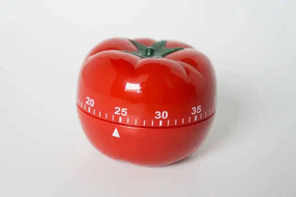 Photo of Close up view of mechanical tomato shaped kitchen clock timer for cooking and studying. Used for pomodoro technique for time and productivity management. Isolated on white background, at 25 minutes.