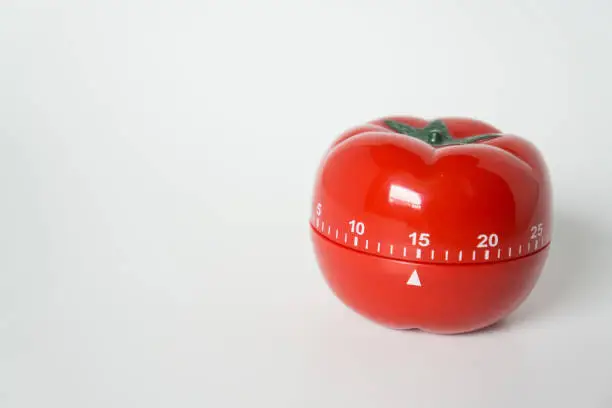 Photo of Close up view of mechanical tomato shaped kitchen clock timer for cooking and studying. Used for pomodoro technique for time and productivity management. Isolated on white background, at 15 minutes.
