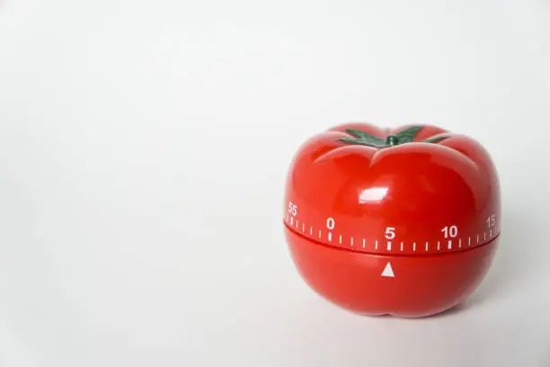 Photo of Close up view of mechanical tomato shaped kitchen clock timer for cooking and studying. Used for pomodoro technique for time and productivity management. Isolated on white background, at 5 minutes.