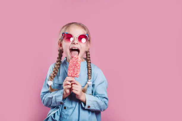 Photo of little cheerful girl in sunglasses with ice cream on pink background