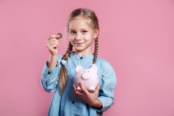 Little girl saving money in a piggybank on pink background stock photo
