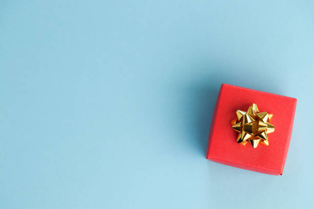 hermosa caja de regalo roja con nudo de arco de oro sobre un fondo azul. concepto de celebración. copiar espacio. estaba plano. - bowknot fotografías e imágenes de stock