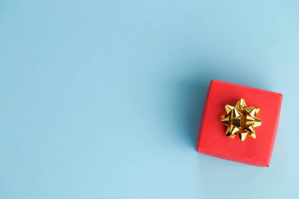 linda caixa de presente vermelha com nó de arco dourado em um fundo azul. conceito de celebração. copiar espaço. lay flat. - bowknot - fotografias e filmes do acervo