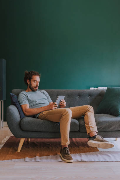 mężczyzna siedzący na kanapie i używający cyfrowego tabletu w domu - sofa men sitting contemporary zdjęcia i obrazy z banku zdjęć