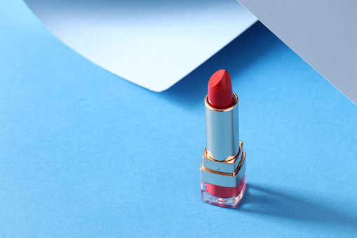 Red lipstick on a blue background with light blue rolled-up paper. Trendy concept. Make up concept. For blogging about beauty and make-up. Red lipstick.