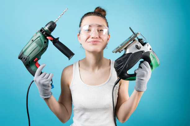 Young woman holds a jigsaw and a drill on a blue background