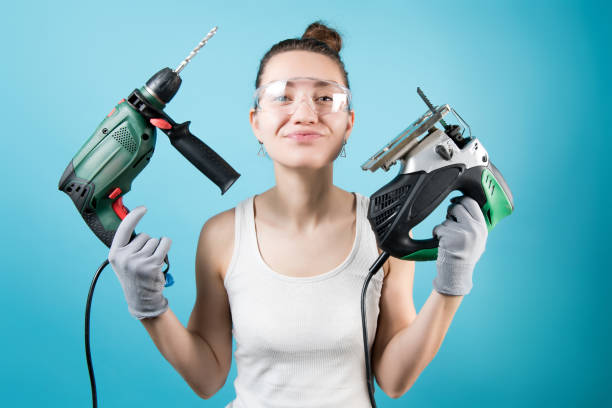 Young woman holds a jigsaw and a drill on a blue background Young woman holds a jigsaw and a drill on a blue background. Isolated on blue womens issues stock pictures, royalty-free photos & images