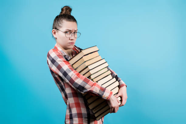 istock Sad young student in eyeglasses holds a large number of books in her hands 1220195607