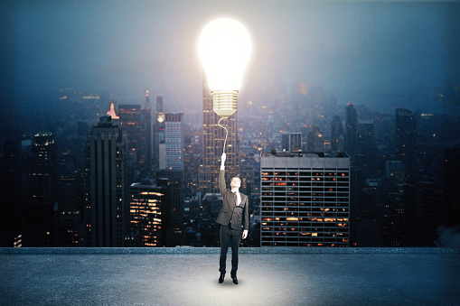 Businessman holding light bulb on city background. Success and startup concept.