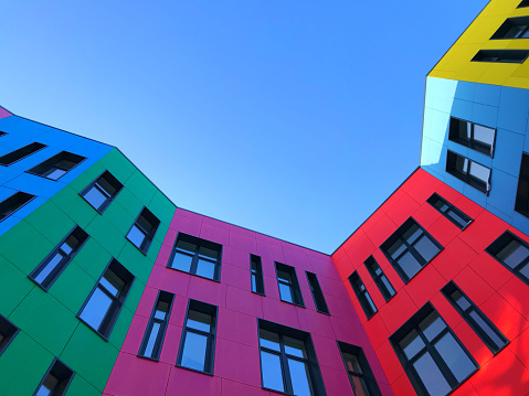 Multi-colored facades of a modern building with black window frames. Look up from the blue sky