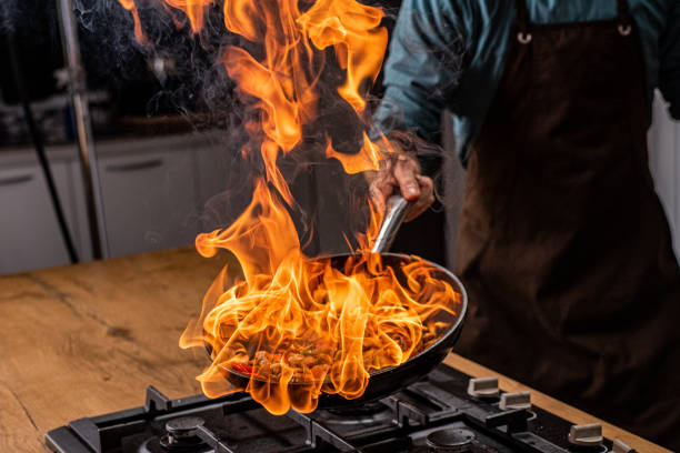 Chef cooking vegetables in pan Close-up of chef's hand flaming vegetables in pan. kitchen on fire stock pictures, royalty-free photos & images