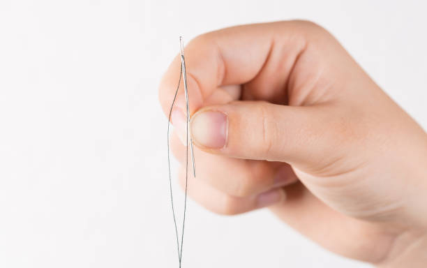 istock Detail of hand holding needle with thread on white background 1220200456