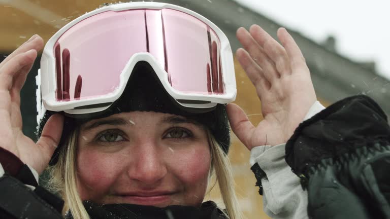 A Smiling Teenaged Female Snowboarder Puts on Her Goggles in Preparation of Snowboarding on an Overcast Winter Day