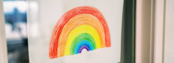 istock COVID-19 rainbow drawing in window displayed for spreading positivity during coronavirus quarantine lockdown. Children giving hope and staying home happy. banner panoramic 1220209762
