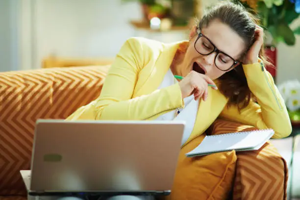 tired elegant student woman in jeans and yellow jacket in the modern house in sunny day study online on a laptop.