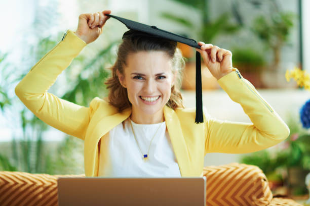 ama de casa moderna feliz con gorra de graduación y portátil - online degree fotografías e imágenes de stock