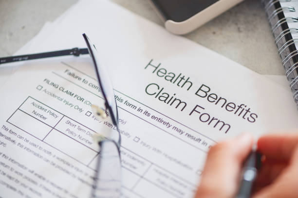 istock Person filling in a health benefits application form. 1220214616