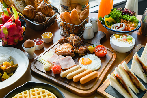 Continental resort breakfast with fried and boiled egg, grilled meat and sausages. Vegetables, croissants, sandwiches, waffles, salad.