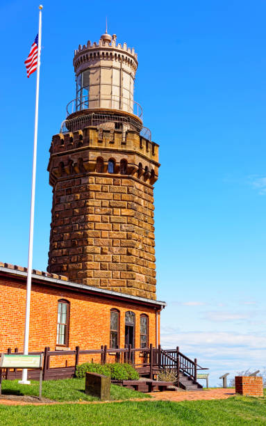Lighthouse with American flag at Atlantic Ocean Bay shore at Sandy Hook. Light house tower is called US Navesink Twin Lights. It is in Highlands in Monmouth County in New Jersey, USA. Blue sky