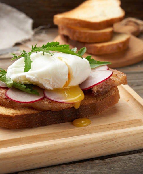 sandwich on toasted white slice of bread with poached eggs, green leaves of arugula and radish