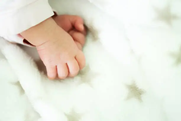 Cover, wallpaper, background photo of small newborn baby fingers on white blanket with stars.