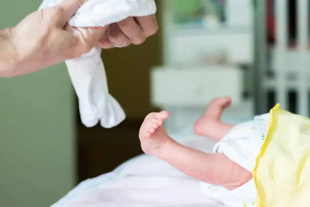 Cropped image of newborn legs and foot and mother hands change baby's clothes and diapers