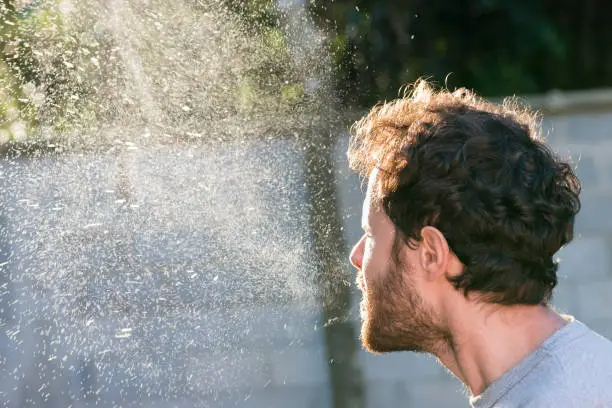 Man sneezing without a mask, sneeze spray cloud  backlight. Airborne germs