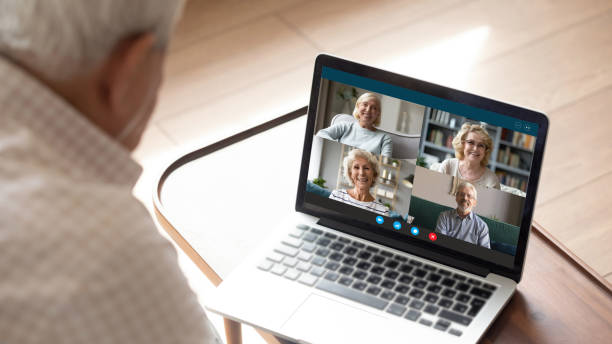 Senior man makes videocall talking with friends by videoconference application Older generation and modern technologies for virtual visual communication concept. Old man makes videocall talking with relatives or friends by video conference app, pc screen view over male shoulder webcam view man stock pictures, royalty-free photos & images
