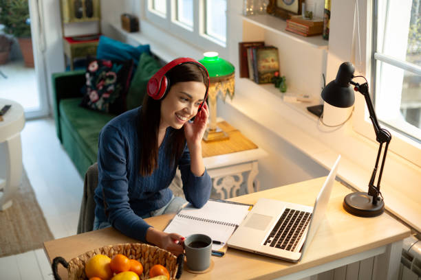 Teaching a class online from home Attractive young woman teacher, teaching by holding an online class with her students from home using her laptop. Having a headphones on and smiling. Relaxed atmosphere and cozy ambient for the improvement of productivity. curfew stock pictures, royalty-free photos & images