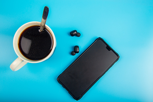 Top view Coffee and smartphone with Wireless bluetooth headphones on a blue background
