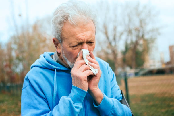istock Elderly man in park blowing nose with handkerchief 1220237792