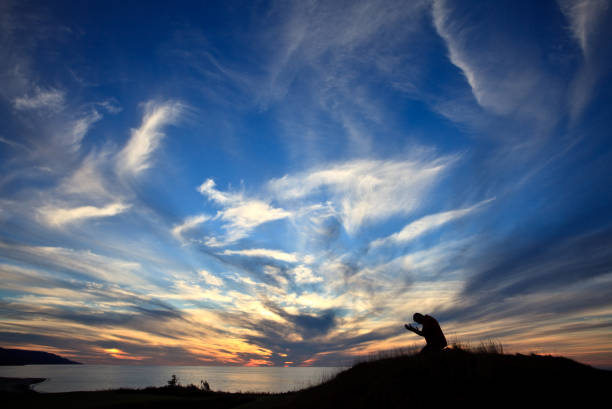 silhouette des menschen auf seinen knien im gebet durch den ozean gegen schönen sonnenuntergang himmel - praying men god kneeling stock-fotos und bilder