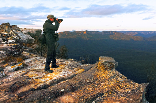 Travel photographer stands on a cliff and photographing the landscape from Lincoln Rock Lookout at sunrise in the Blue Mountains National Park in New South Wales, Australia.