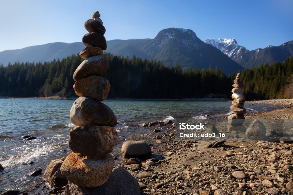 Girl in Canadian Nature Balancing Rocks on the beach by the Alouette Lake during a sunny winter day. Taken in Golden Ears Provincial Park, near Vancouver, British Columbia, Canada. Alouette Lake Stock Photo
