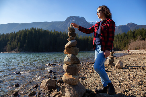 Girl with Balancing Rocks on the beach by the Alouette Lake during a sunny winter day. Taken in Golden Ears Provincial Park, near Vancouver, British Columbia, Canada.