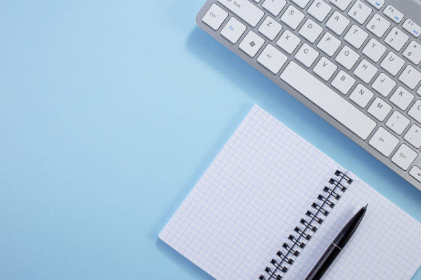 Minimal work space. Creative flat lay photo of workspace desk. Top view office desk with notepad, keyboard, paper notepad and supplies on blue color background. Work from home idea.