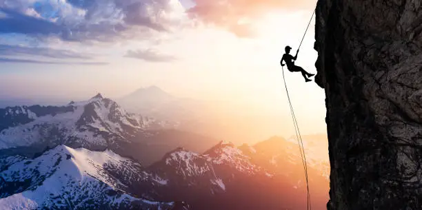 Adventure, Explore Concept Composite. Silhouette Rappelling from Cliff. Beautiful aerial view of the mountains during a colorful and vibrant sunset or sunrise. Landscape taken in Washington, USA.