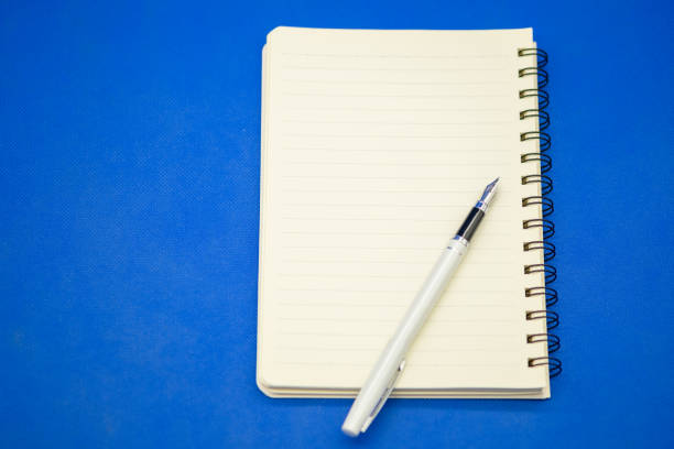 istock Closeup of pen on white book on blue background with copy space for text. 1220271309
