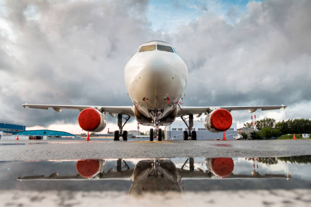 istock White passenger jet plane parked near the hangars with reflection in a puddle. Front view 1220272930