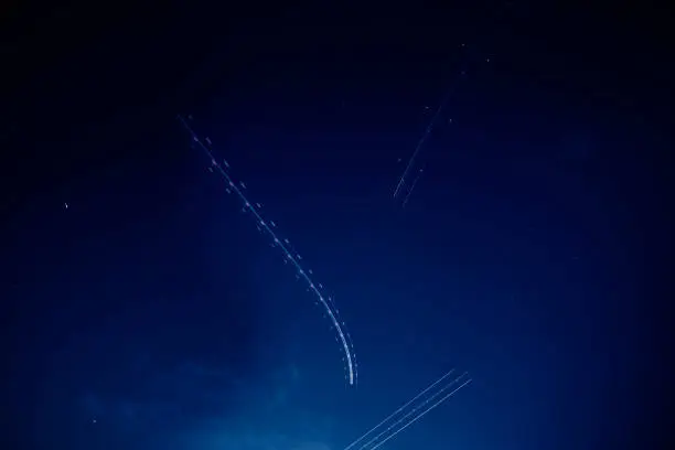 Photo of Multiple flying Airplane light trails blinking in the dark sky long exposure photography