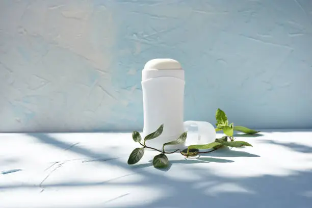 Photo of White bottle of dry deodorantat and green branch at blue concrete wall