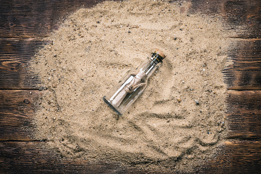 Ancient letter scroll in the glass bottle on the sand on the wooden flat lay table background.