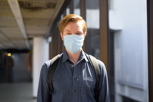 Portrait of young tourist man travelling with mask for protection from corona virus outbreak at the airport