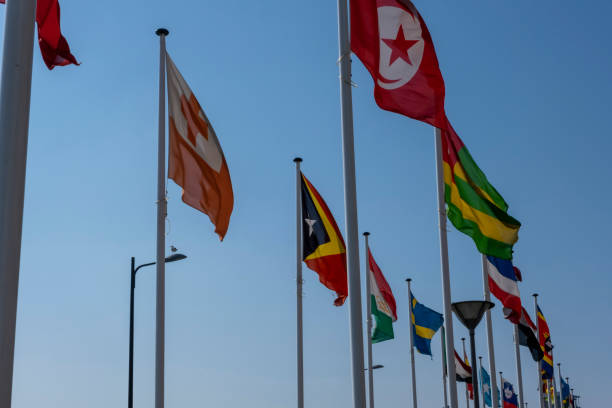 istock Flags waving in the wind on flagpoles equal distant apart against a blue sky 1220277593