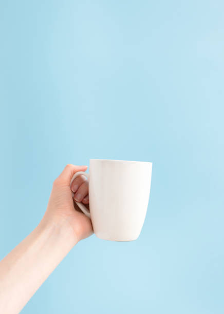 istock Woman holding white cup on blue background and copy space, vertical. Template mockup mug in hand 1220280238