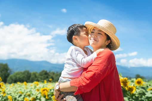 Asian mother carrying her son in front of sun flower fields.