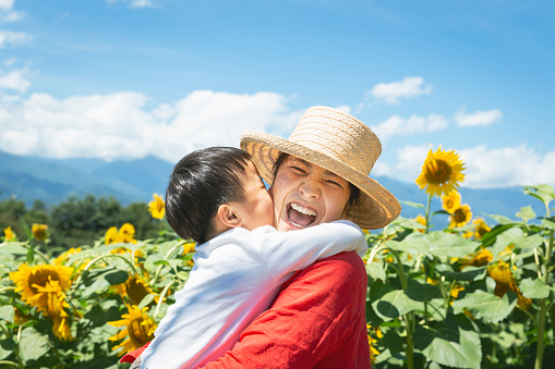Asian mother carrying her son in front of sun flower fields.