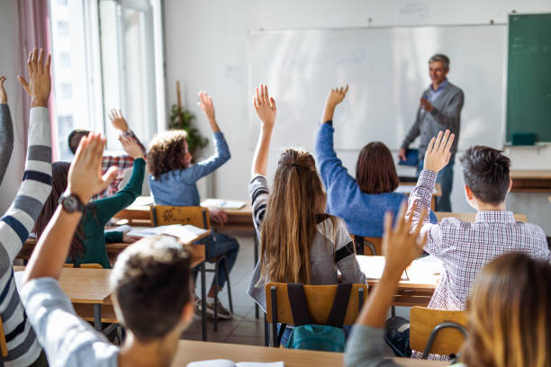 istock Back view of  high school students raising hands on a class. 1220280990