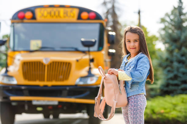 little girl standing by a big school bus door with her pink backpack. - blond hair carrying little girls small imagens e fotografias de stock
