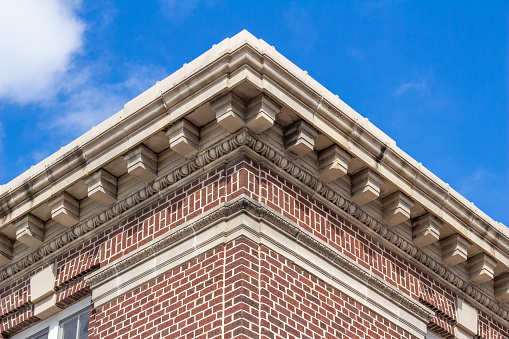 This image shows a close-up upward abstract view of the decorative cornice on a vintage red and white brick building, with blue sky background.